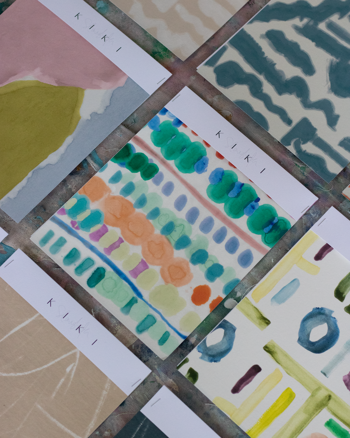 Collection of cards with abstract designs and 'KIKI' branding on a textured surface.