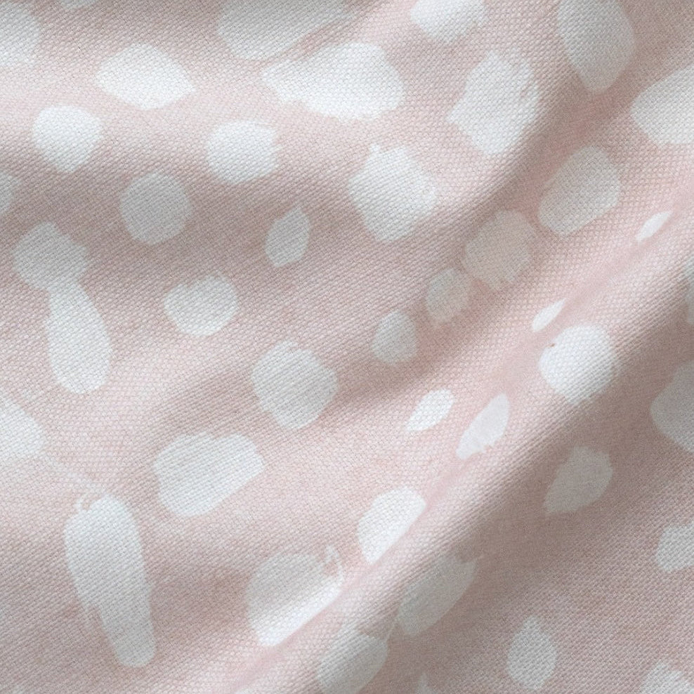 A fabric with a blush pink background featuring an organic pattern of white dots.