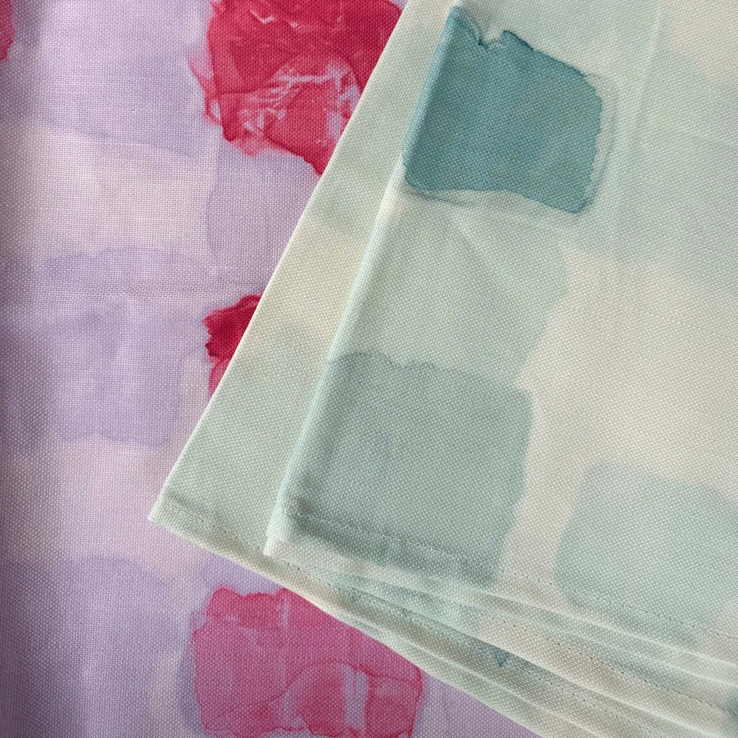 Close-up of a fabric with abstract patterns in pink, red, and green on a light purple background.