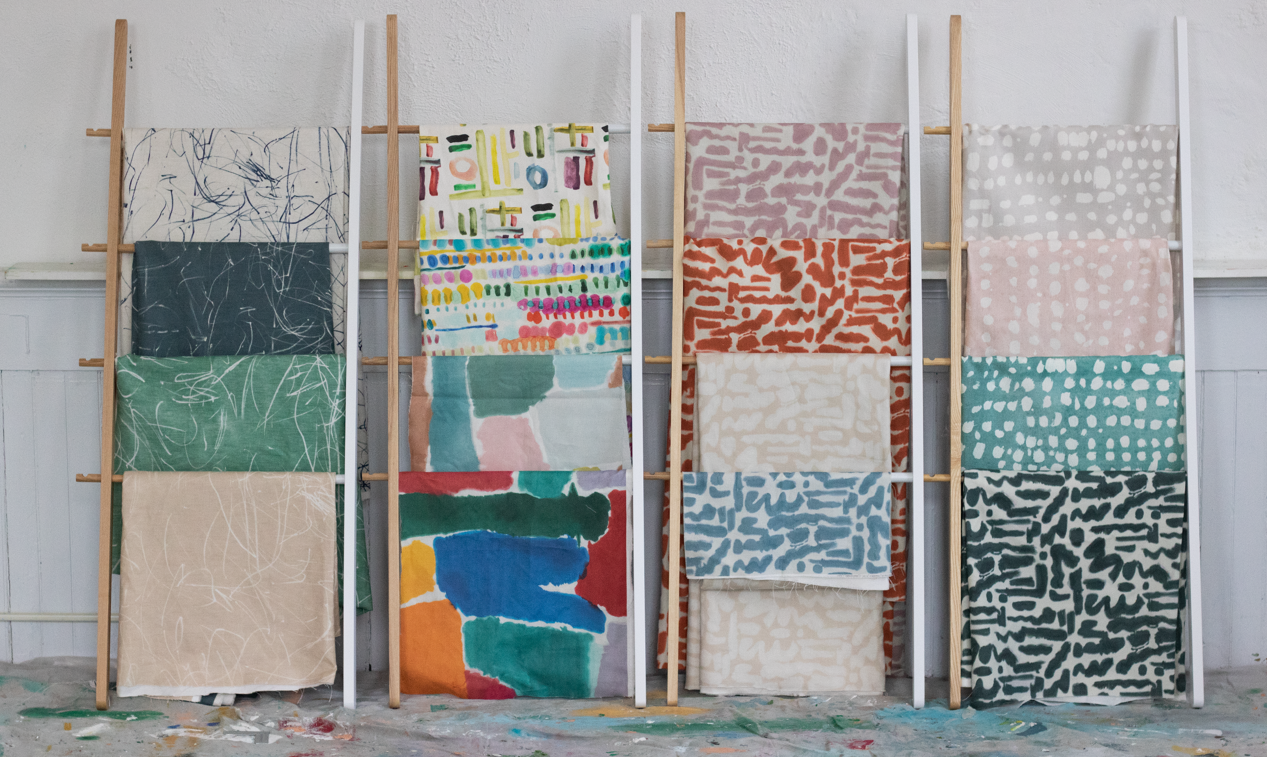 Four fabric samples on a wooden ladder against a white wall.