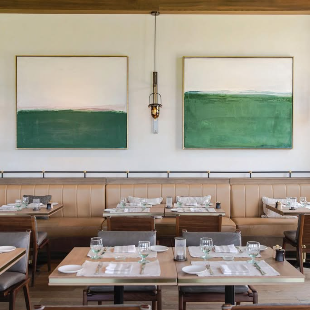 Modern restaurant interior with wooden tables, chairs, and abstract green paintings on the wall.