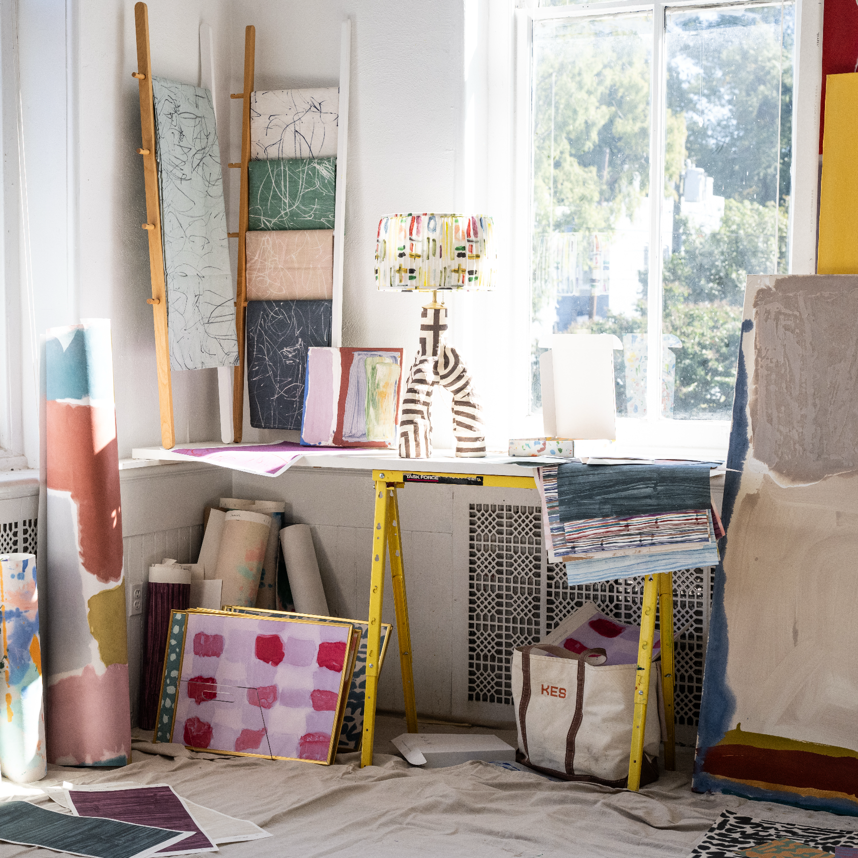 Art studio with various art supplies and canvases on a table by a window.